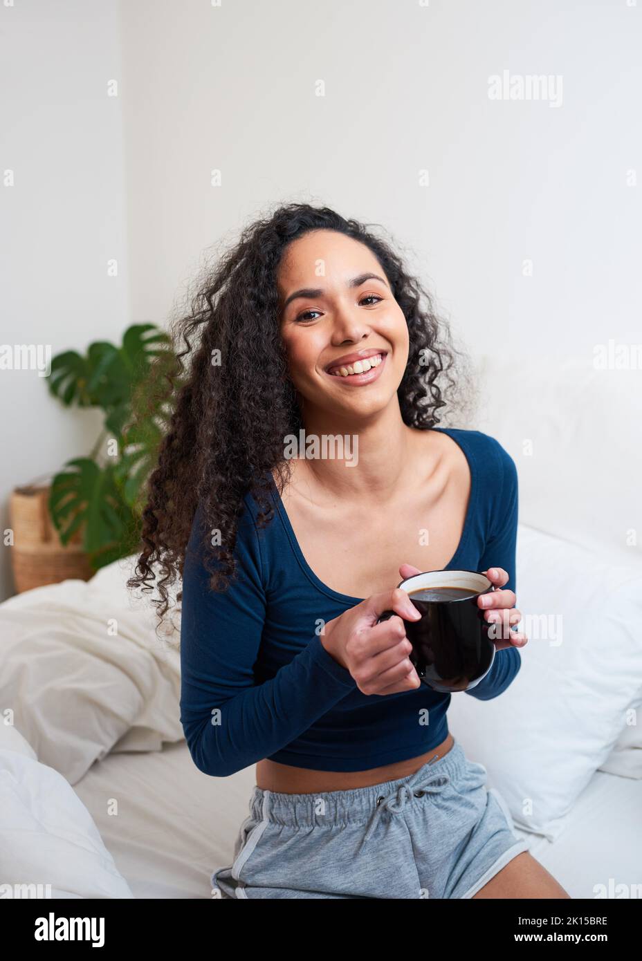 Una giovane donna felice multi-etnica si sveglia bevendo caffè in camera da letto Foto Stock