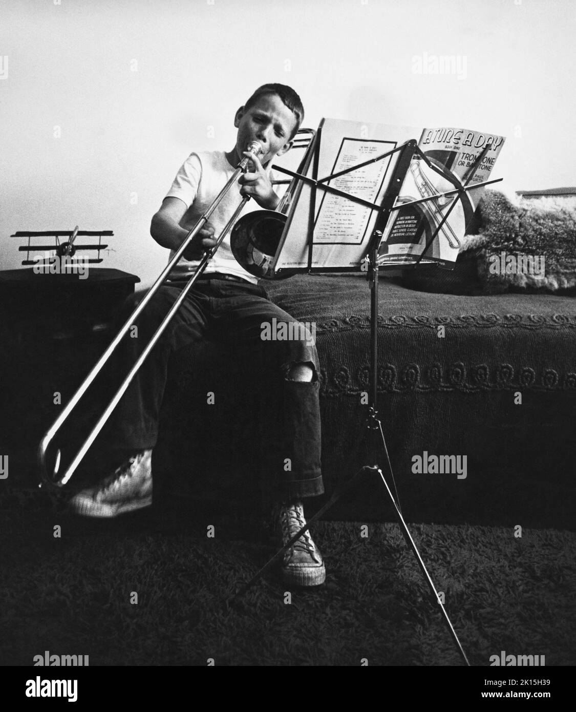 L'immagine storica di un ragazzo che impara a giocare il trombone nella sua camera da letto. Foto Stock