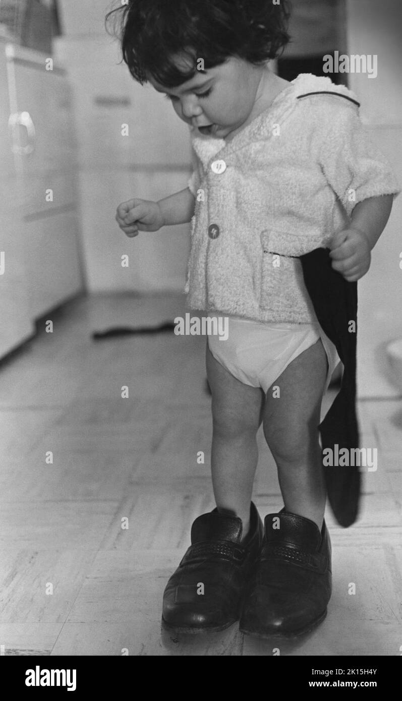 Un ragazzo di 18 mesi è fotografato nelle scarpe del padre; circa 1976. Foto Stock