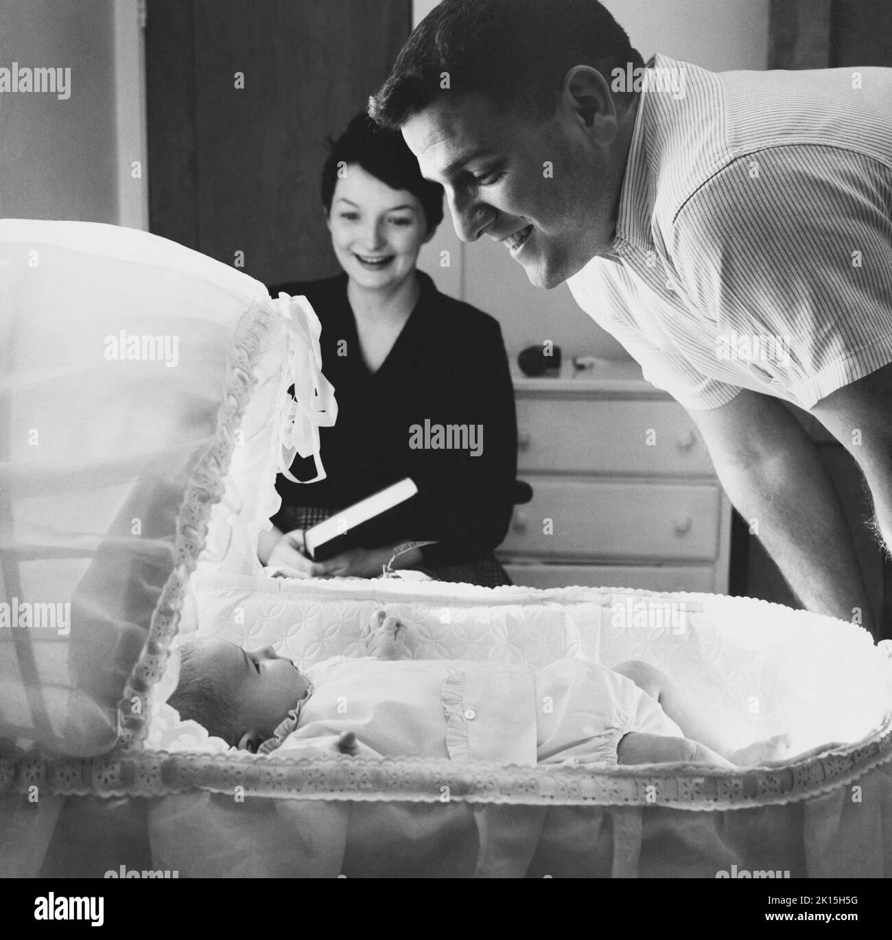 I genitori sorridenti ammirano il loro neonato. 1958 Foto Stock