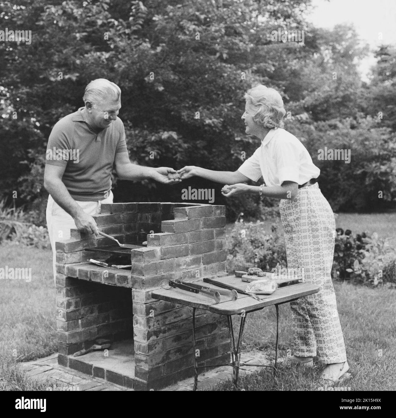 Una coppia anziana godendosi l'azienda dell'altro mentre cucinano fuori nel loro cortile. Foto Stock