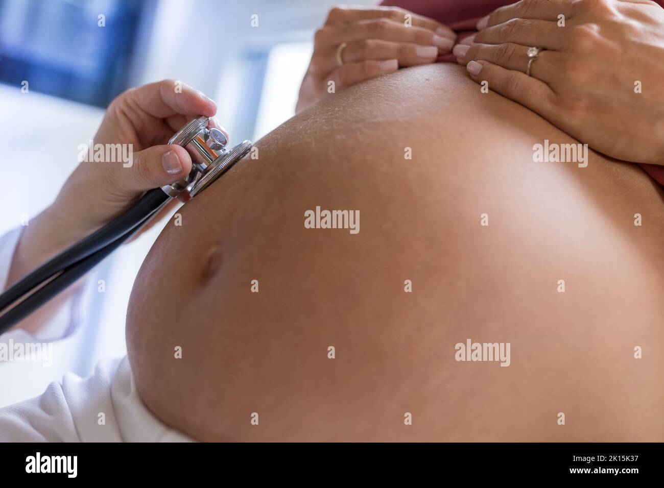 Primo piano della pancia della donna incinta e della mano del medico con lo stetoscopio che ascolta il cuore del bambino Foto Stock