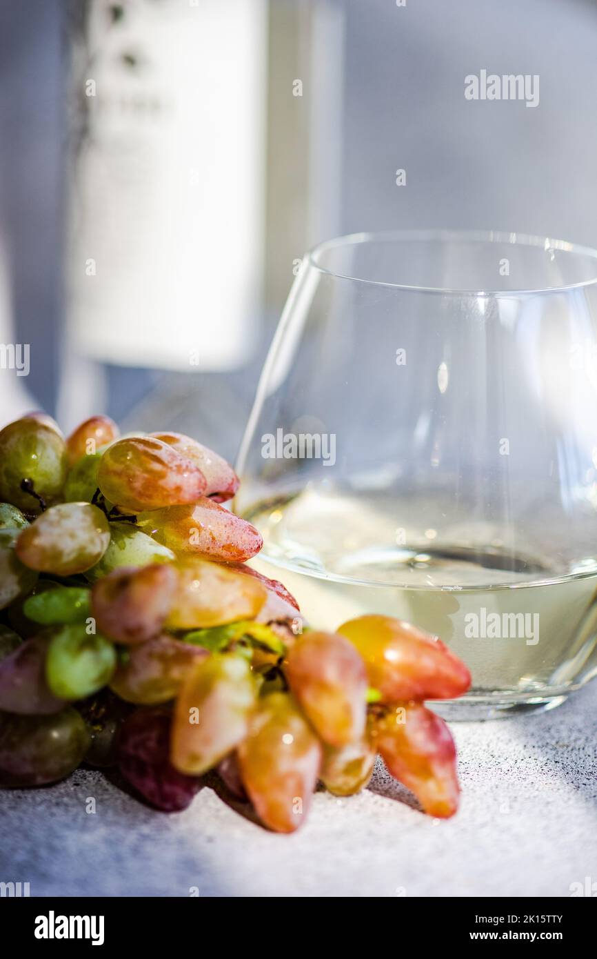Vino bianco secco in vetro e uve mature su fondo grigio Foto Stock