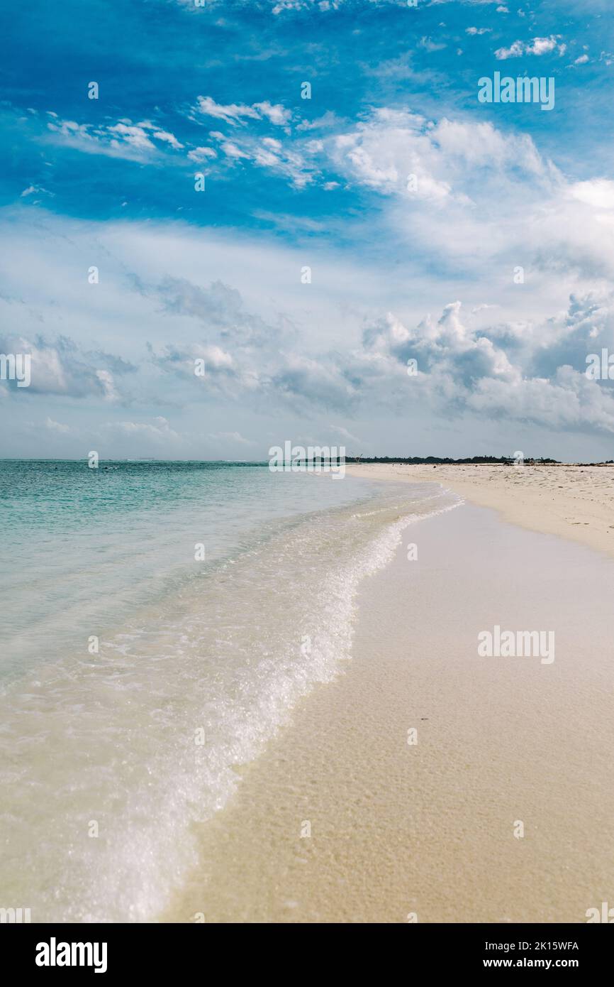 Onde trasparenti di acqua di mare pulita che rotola sulla spiaggia sabbiosa dell'isola di Thulusdhoo contro il cielo blu nuvoloso nelle Maldive Foto Stock
