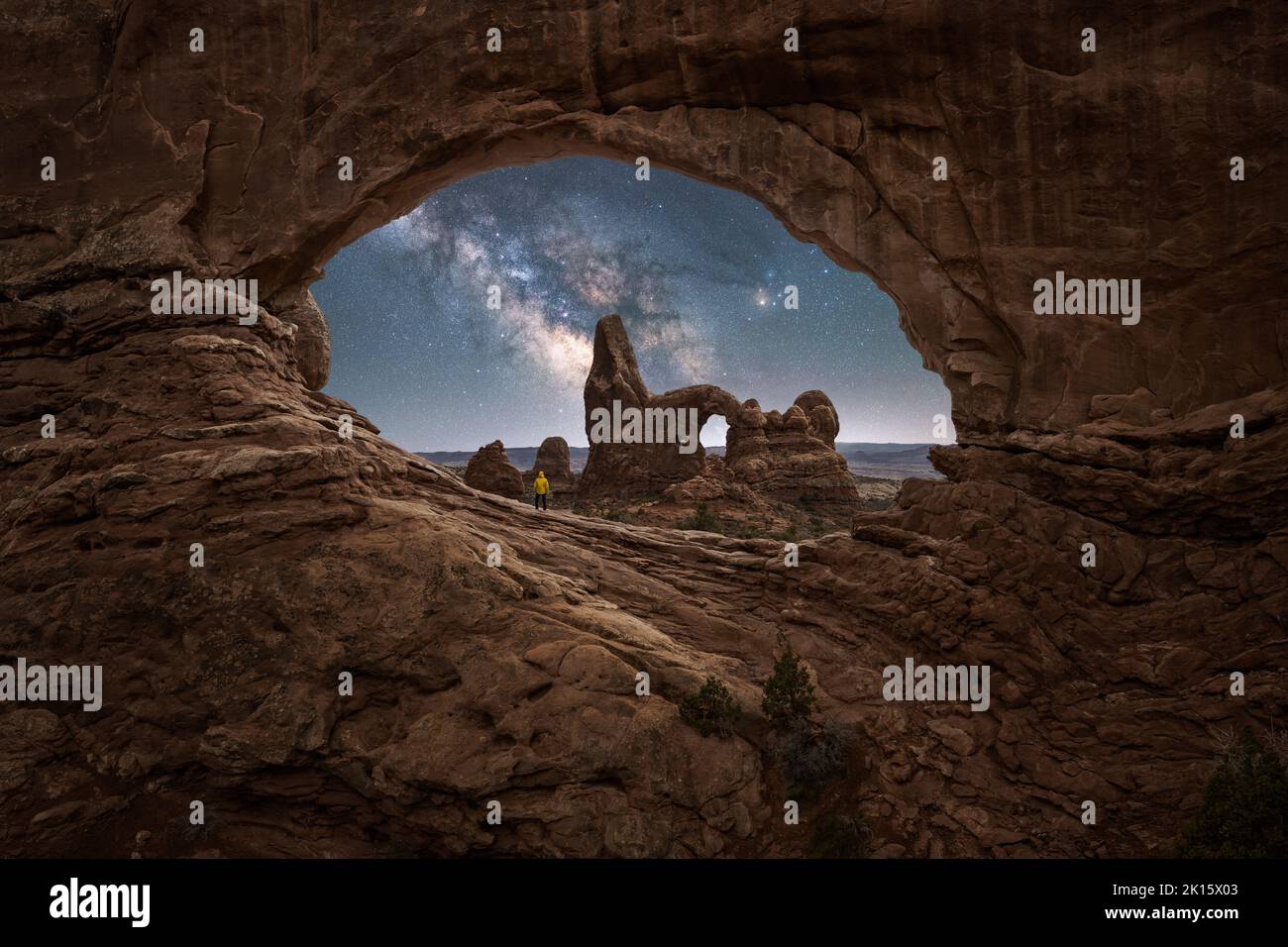 Un viaggiatore irriconoscibile che ammira la vista mozzafiato di Turret Arch, situato vicino a un canyon ruvido contro la Via Lattea scintillante al cielo notturno in Arches National Foto Stock