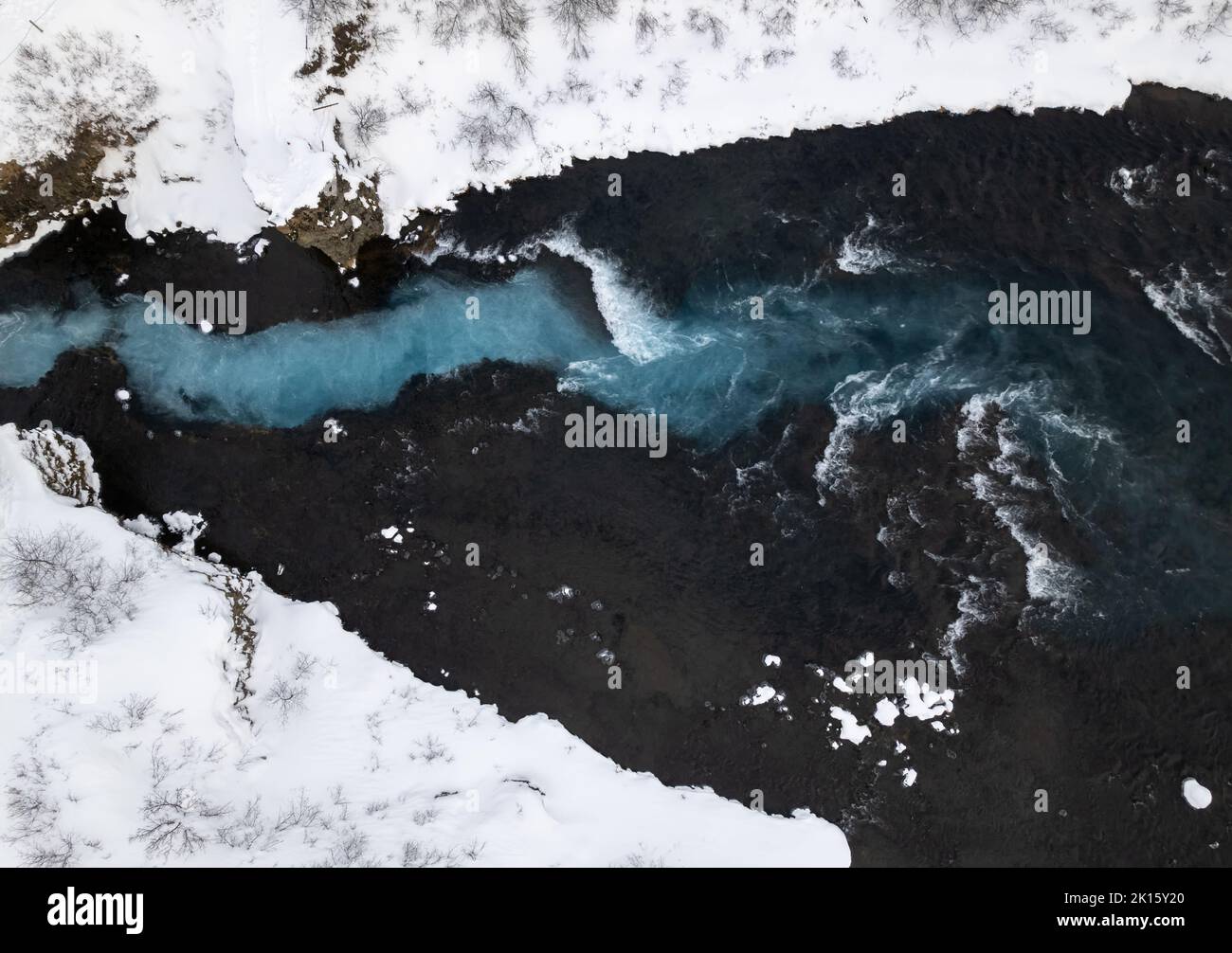 Vista aerea dall'alto delle onde di mare schiumose che si tuffano su una costa rocciosa e rocciosa ricoperta di neve nella fredda giornata invernale in Islanda Foto Stock