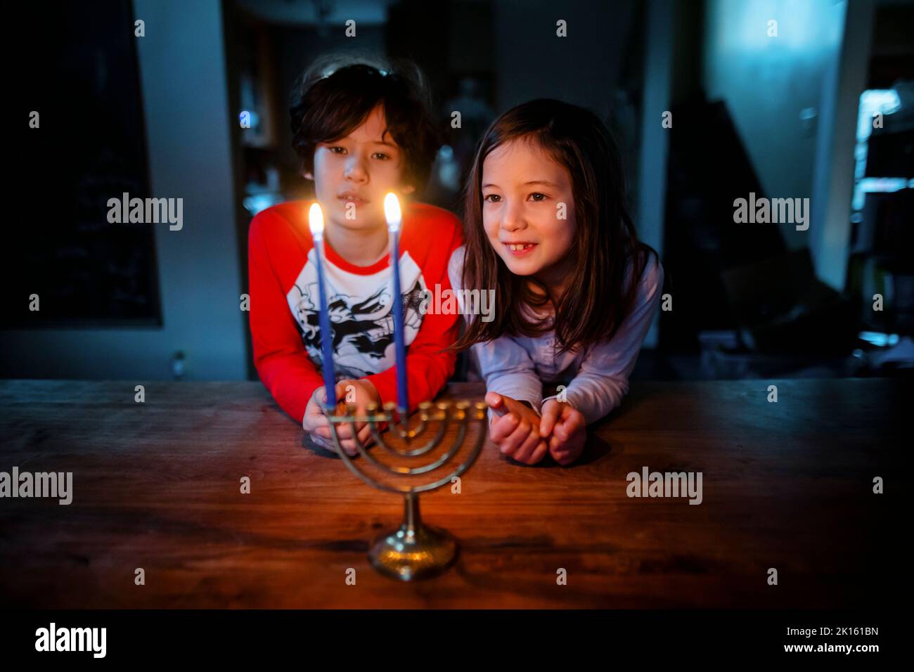 Due bambini si siedono insieme a tavola guardando la menorah illuminata ad Hannukah Foto Stock