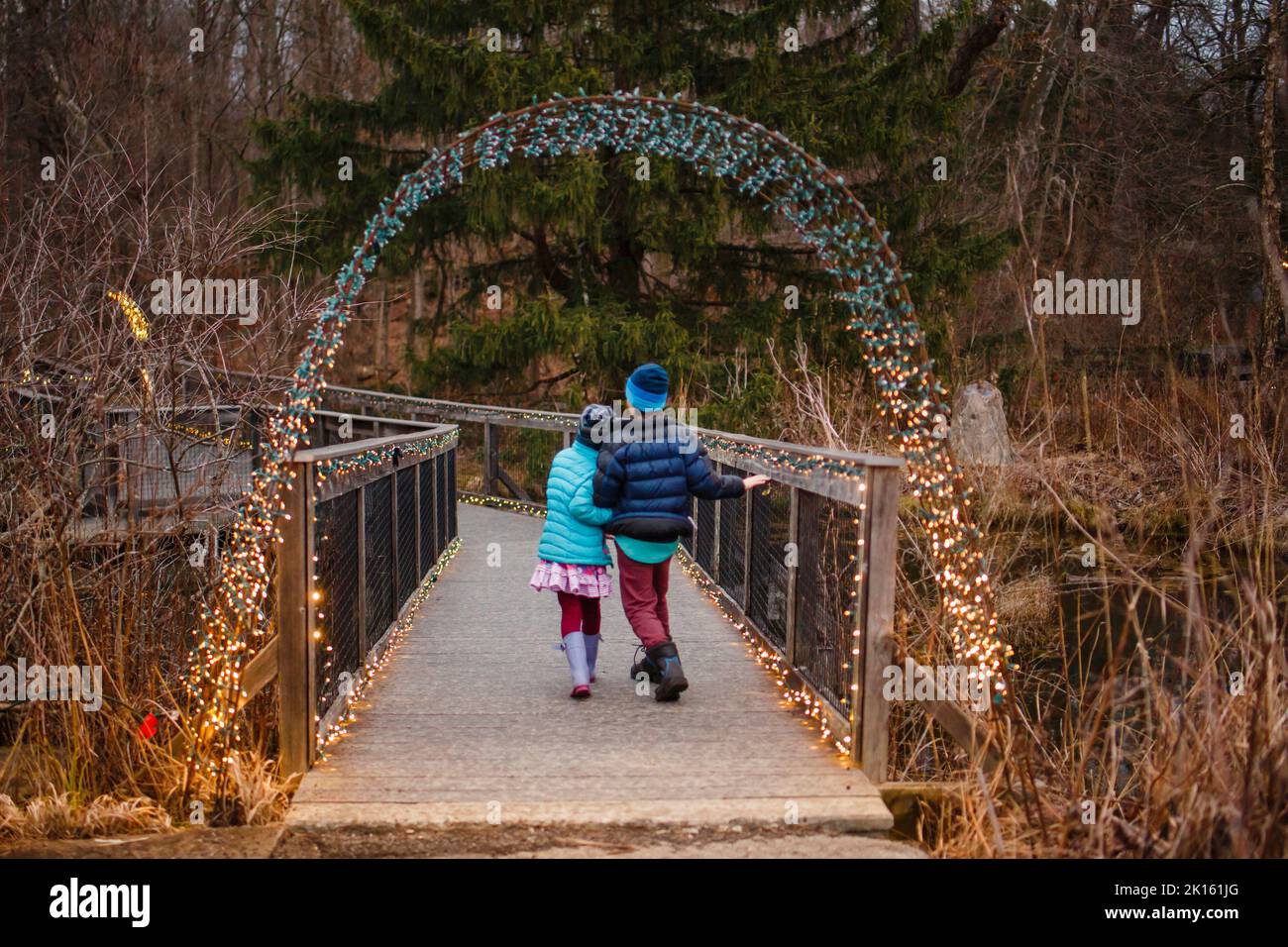 Due bambini camminano lungo un sentiero attraverso boschi illuminati dalle luci natalizie Foto Stock