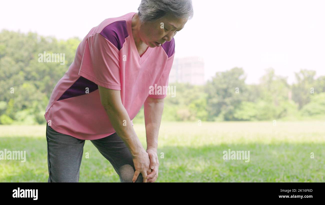 Donna anziana che sente dolore al ginocchio mentre si esercita nel parco Foto Stock