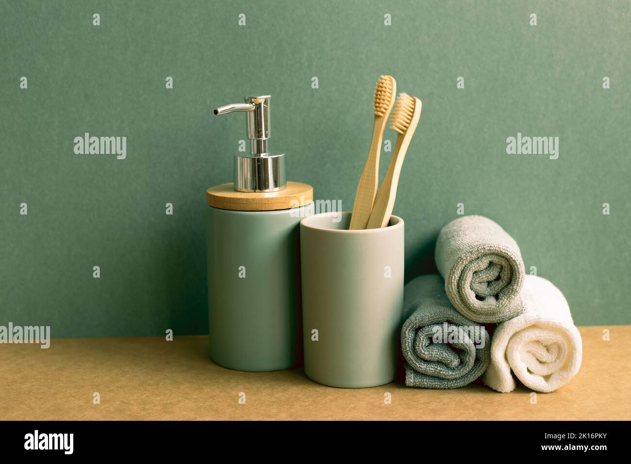 Sapone, bottiglia di shampoo e asciugamani in cotone, spazzolino da denti su ripiano marrone. Sfondo parete verde. Interno bagno Foto Stock