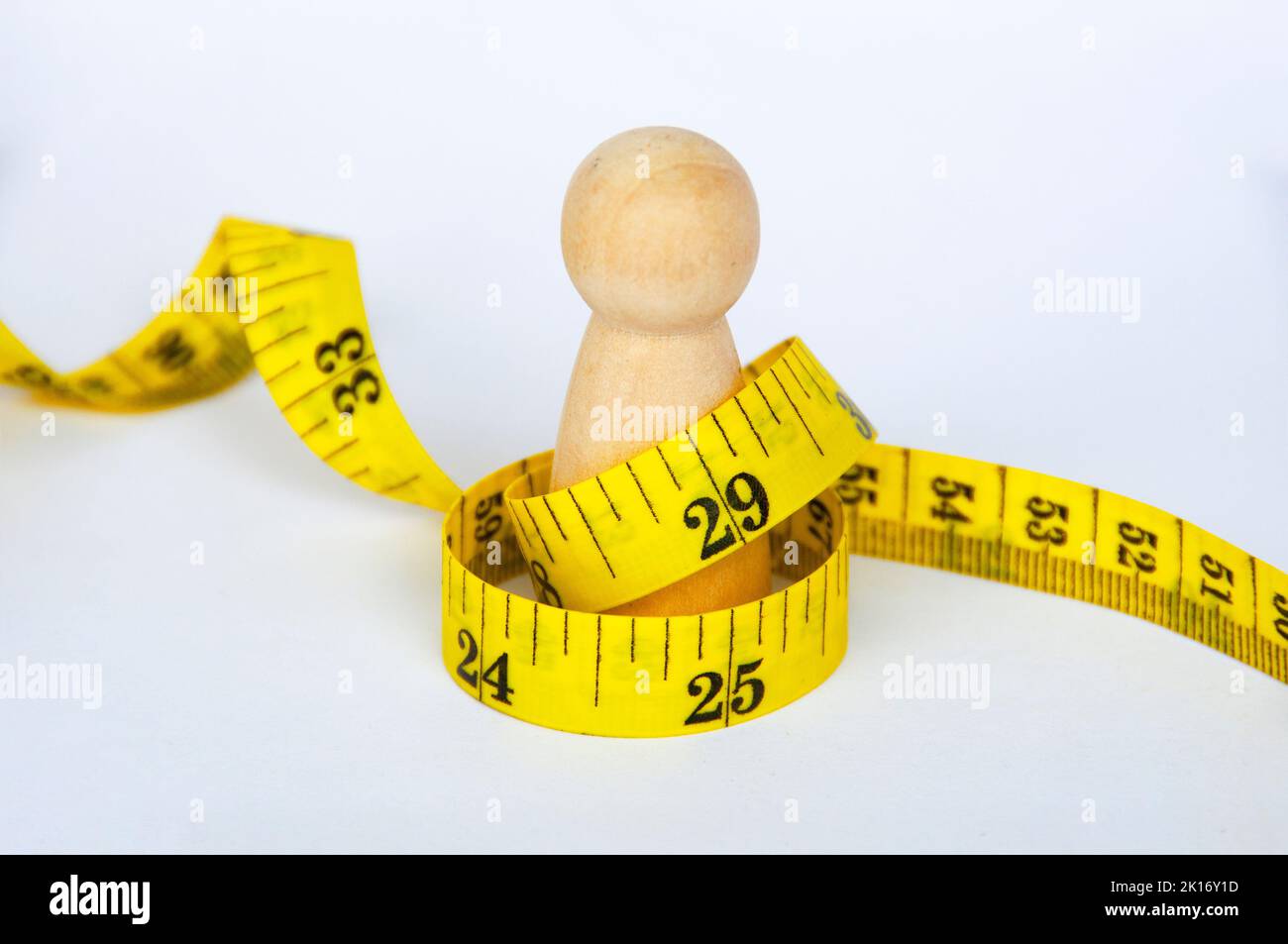 Bambola di legno avvolta con nastro di misurazione giallo su sfondo bianco. Concetto di perdita di spazio e peso della copia. Foto Stock