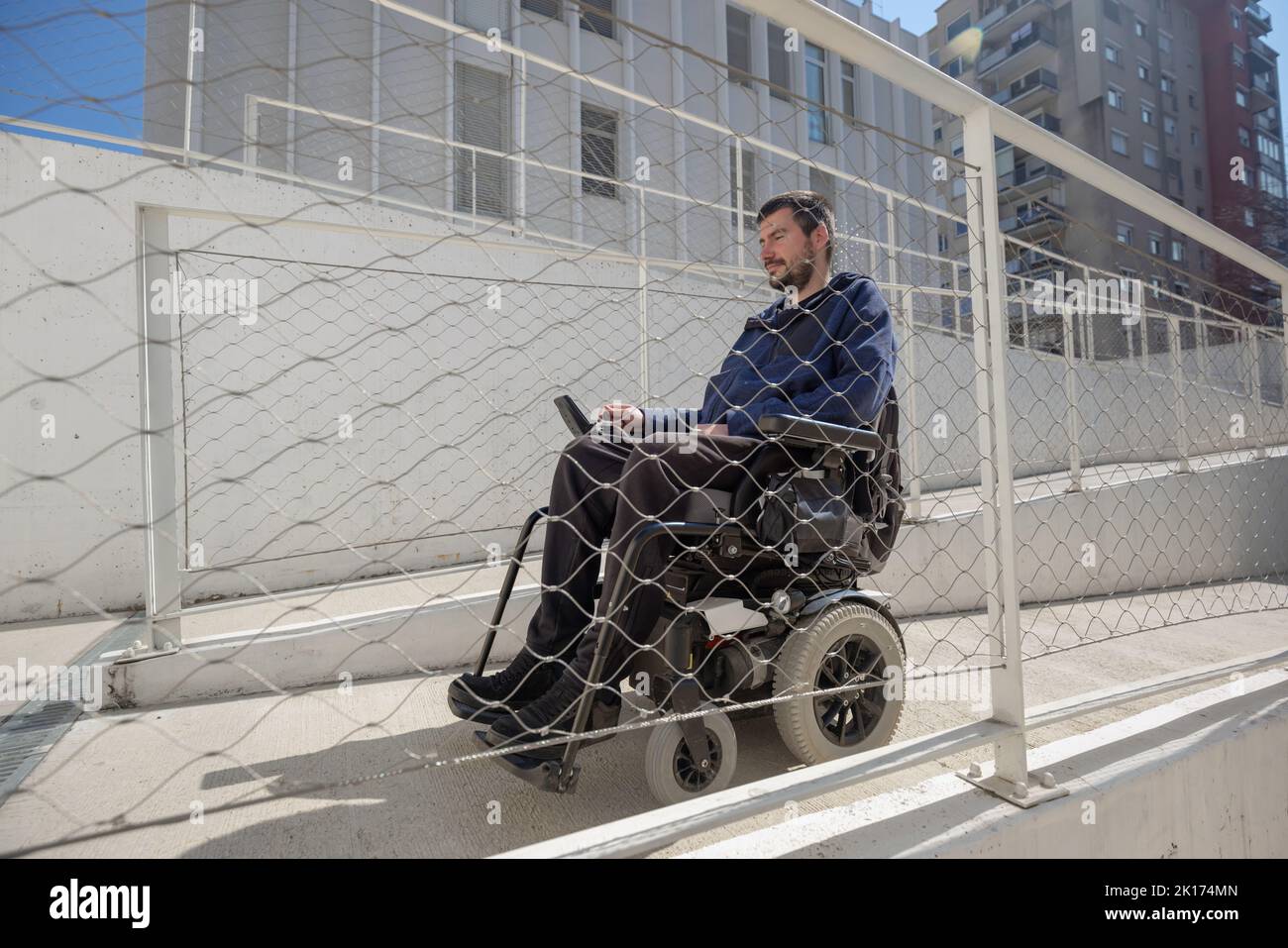 Uomo su sedia a rotelle, in avvicinamento all'edificio che si sposta lungo una rampa accessibile per persone con disabilità Foto Stock