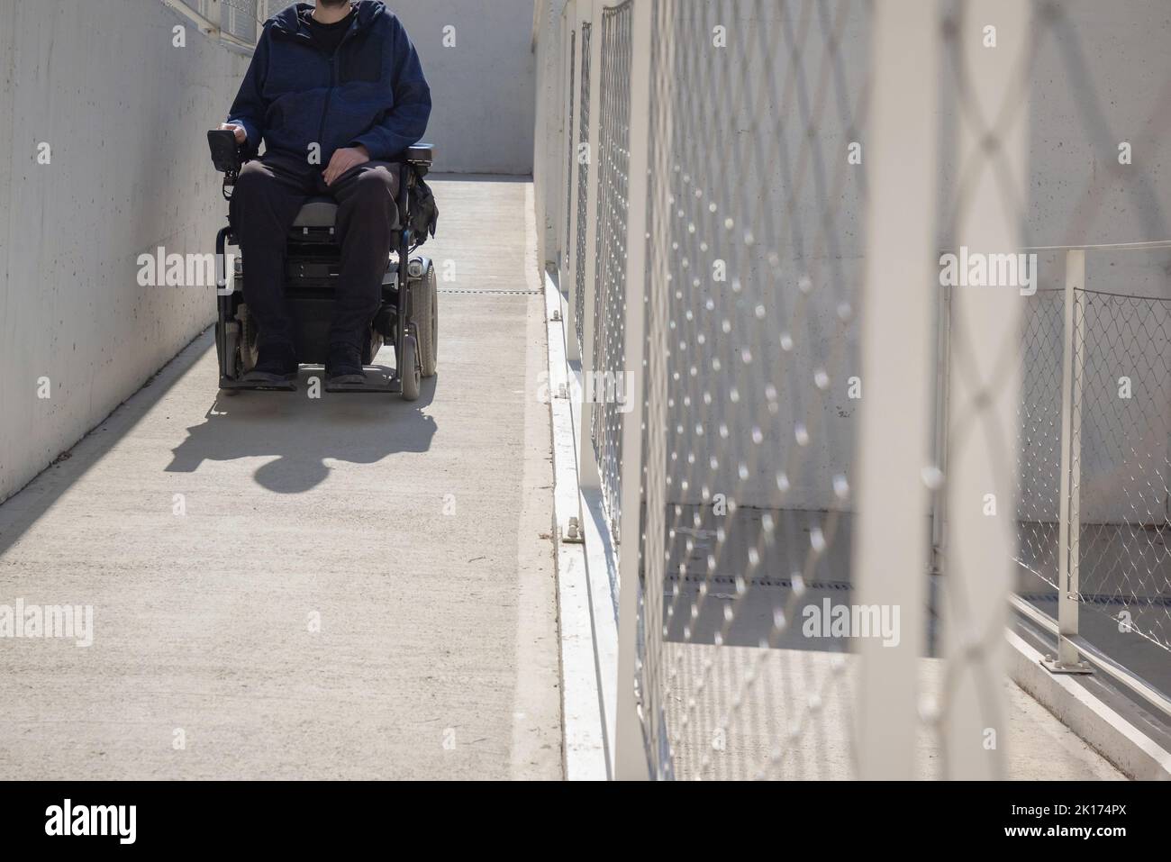 Uomo su sedia a rotelle, in avvicinamento all'edificio che si sposta lungo una rampa accessibile per persone con disabilità Foto Stock