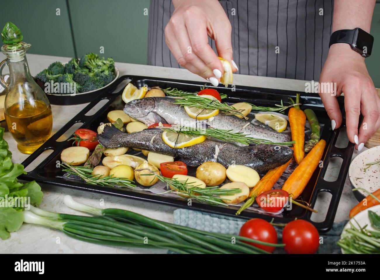 Donna che prepara pesce branzino con erbe aromatiche, verdure e limone per cucinare alla griglia Foto Stock
