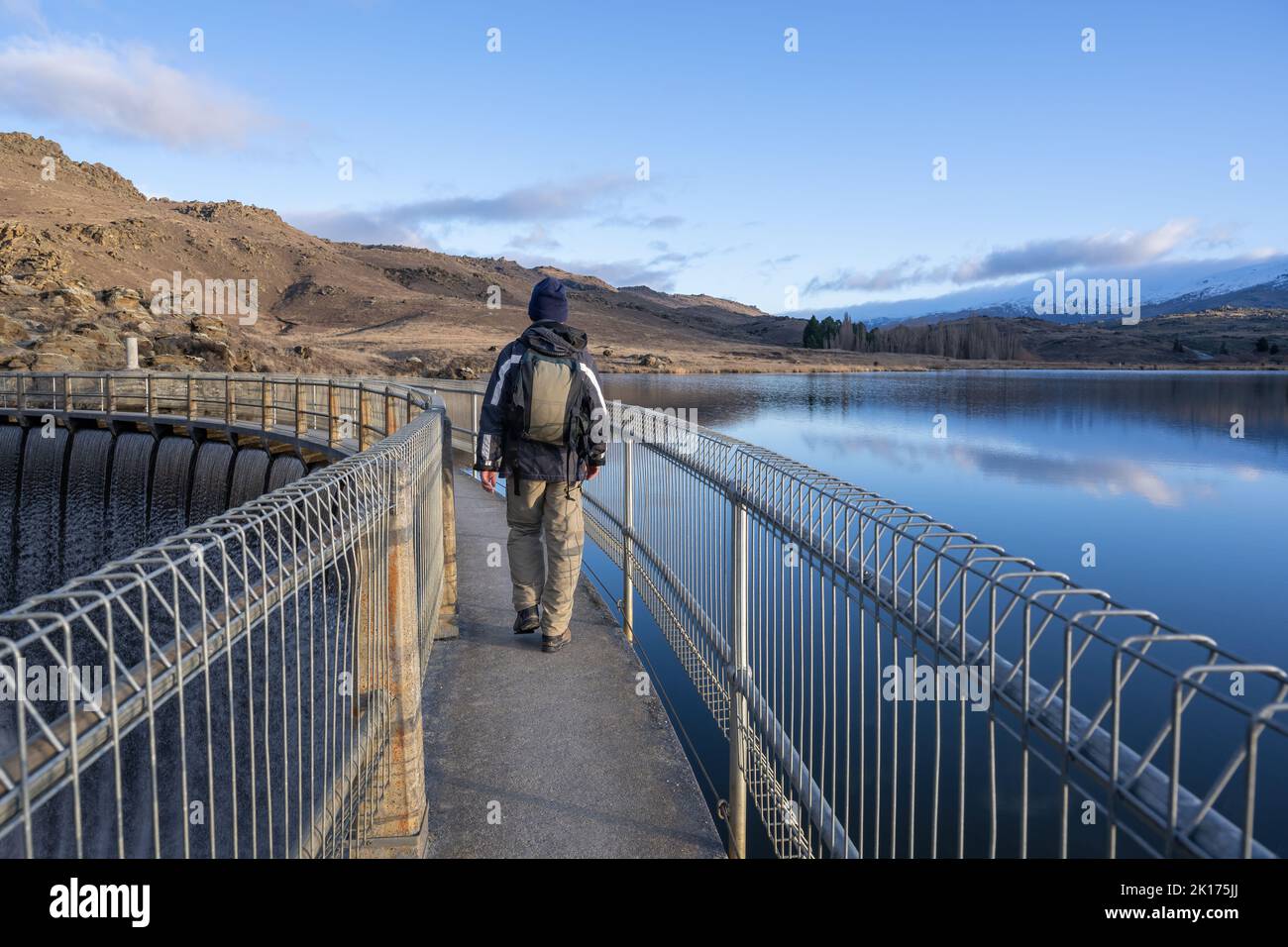 Uomo che cammina sulla pista ad anello della Butchers Dam. L'acqua cade sulle vie di fuoriuscita. Alexandra, Otago centrale. Foto Stock