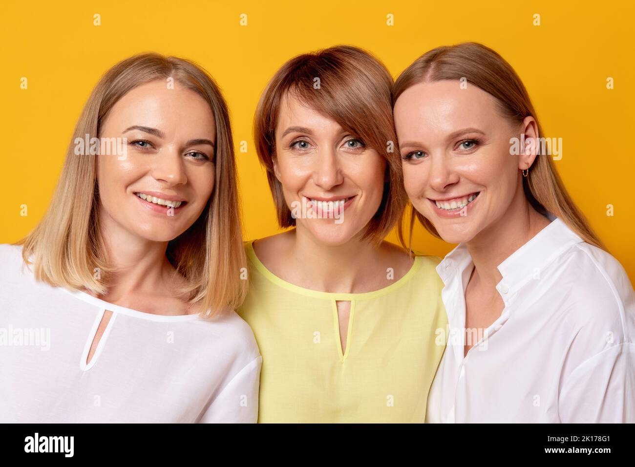 Felicità femminile. Bellezza benessere. Amore sostegno. Ritratto di tre donne positive in blusa bianca gialla insieme sorridendo isolato su sfondo arancione Foto Stock