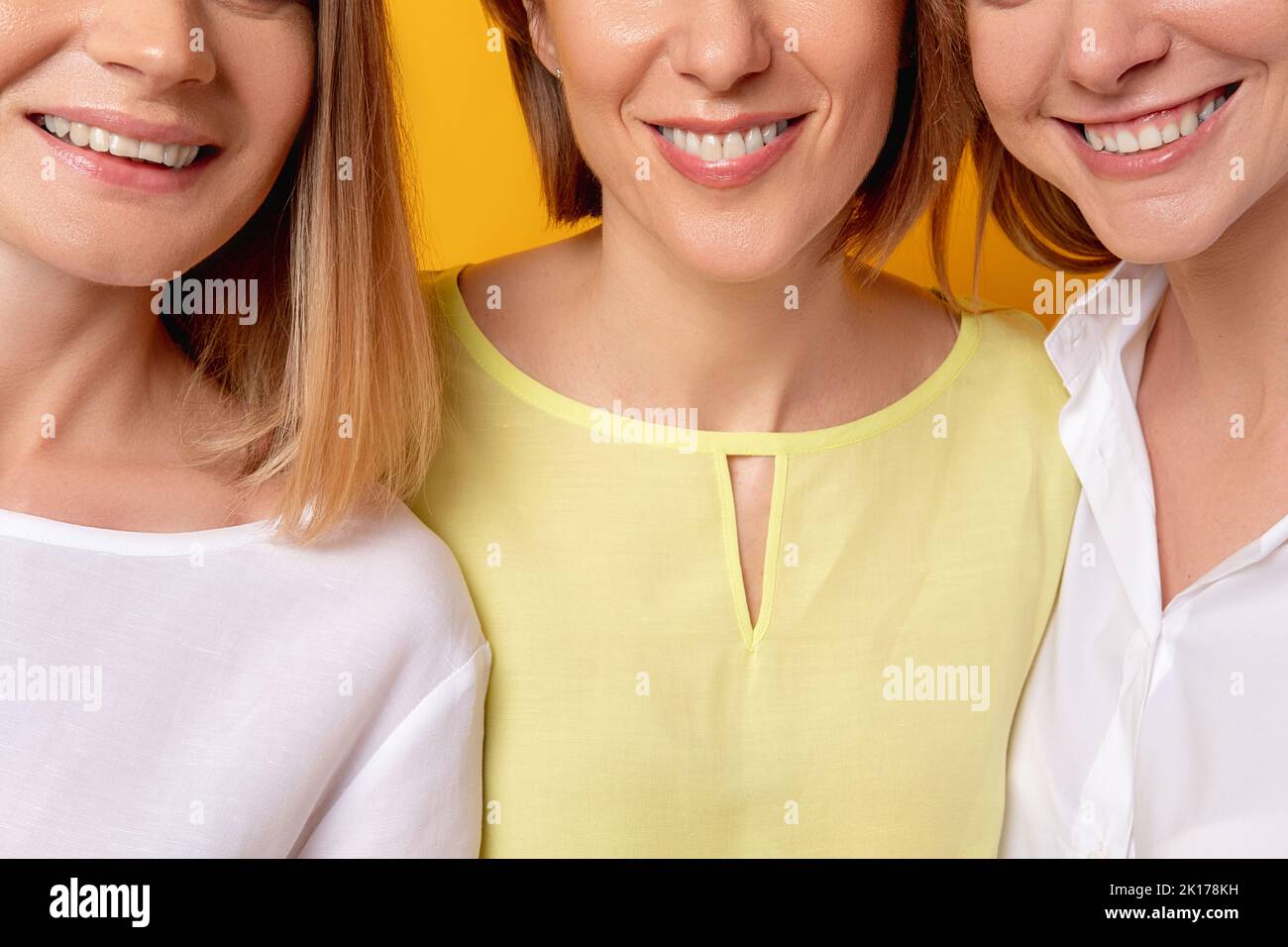 Sorriso toothy. Salute dentale. Bellezza femminile benessere. Ritratto corto di tre donne positive felici soddisfatte in blusa bianca gialla insieme sorridente Foto Stock