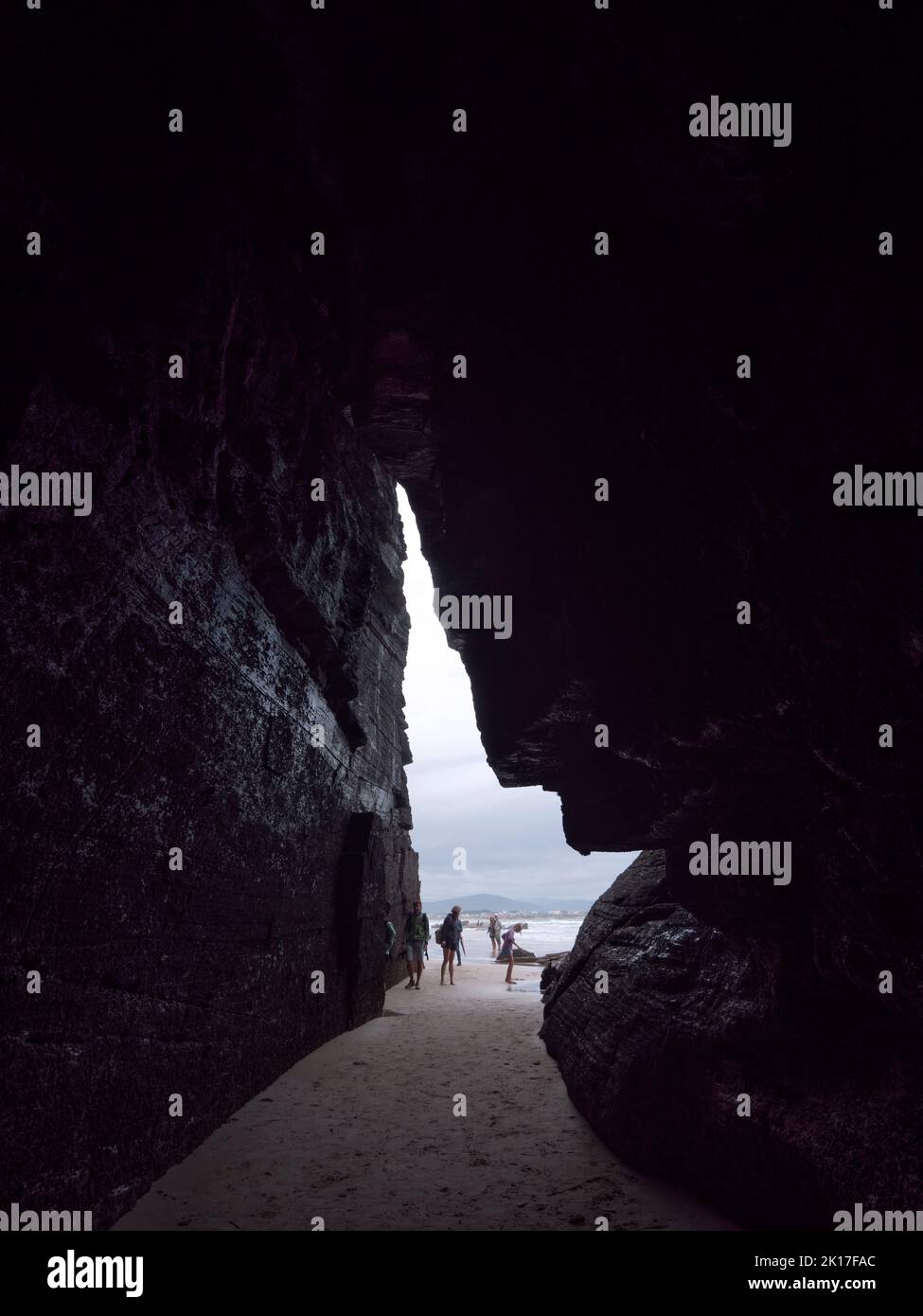 Turisti all'ingresso di una grotta sulla spiaggia in bassa marea. Foto Stock