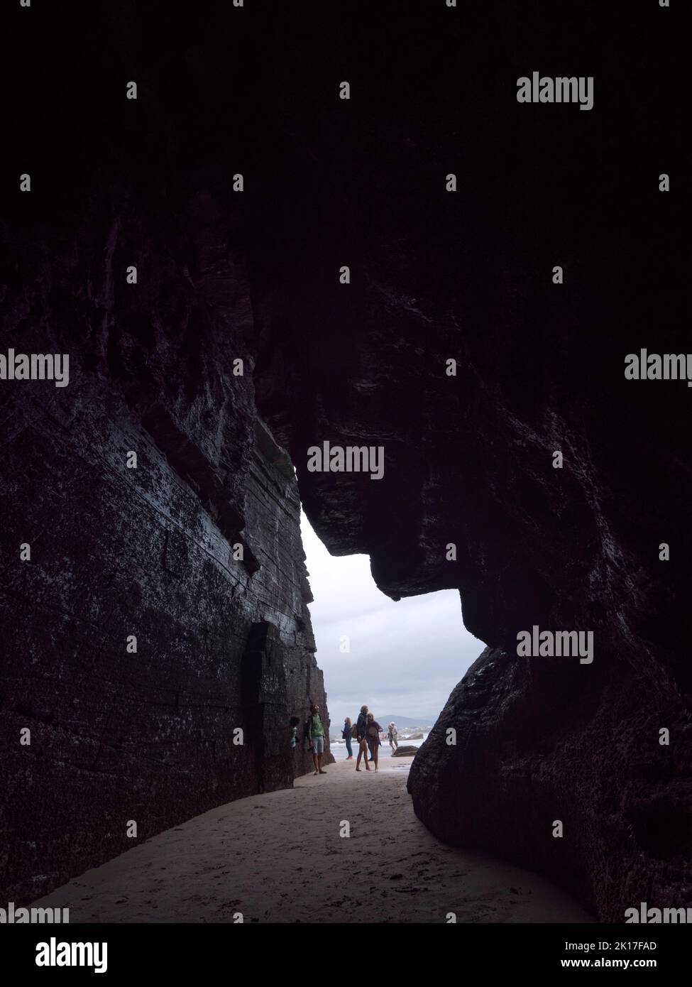 Turista che entra in una grotta di spiaggia scura nella bassa marea. Foto Stock