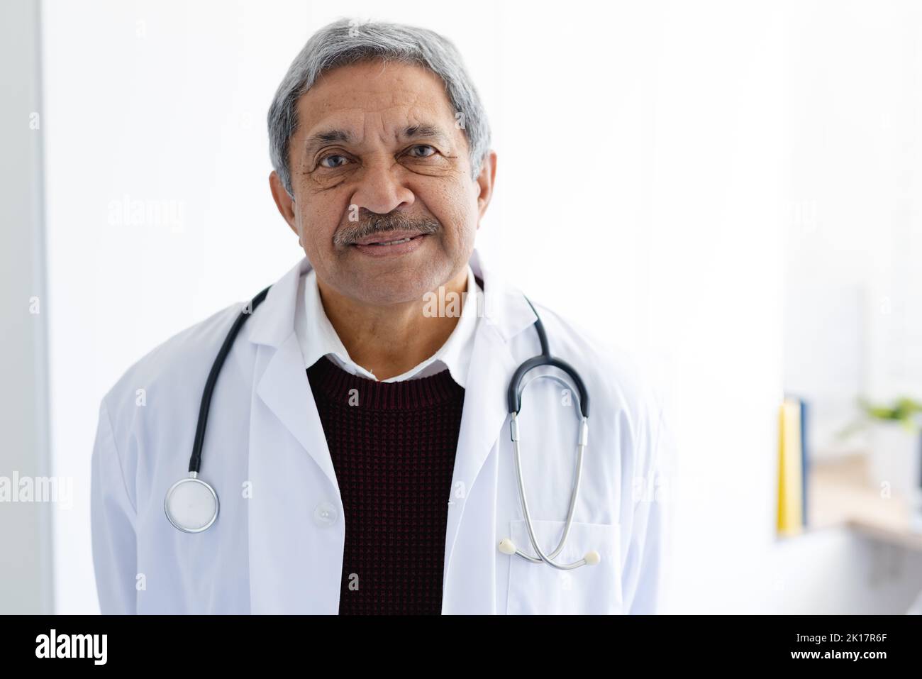 Ritratto di medico biraciale anziano sorridente con stetoscopio con mantello bianco Foto Stock