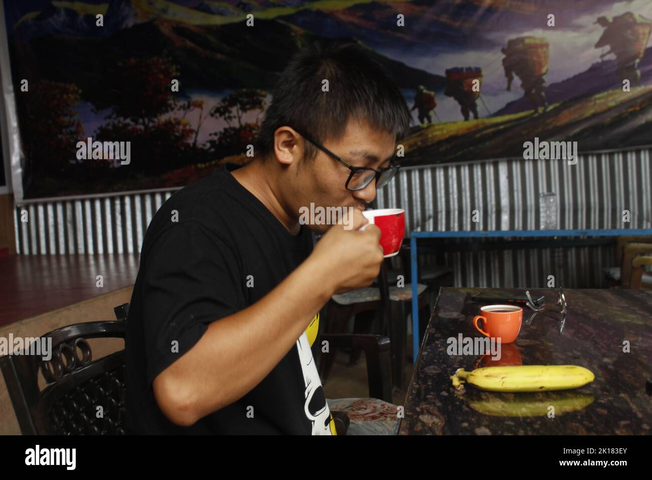 Un ragazzo indossa un bicchiere e beve il tè al mattino, mette una banana, mangia frutta Foto Stock