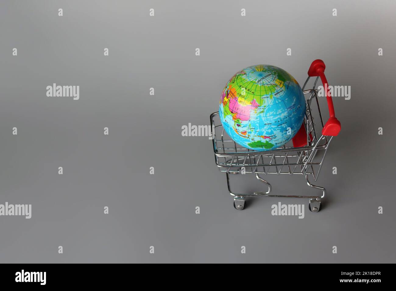 Mercato globale, concetto di mercato internazionale. Mini carrello e globo su sfondo grigio Foto Stock