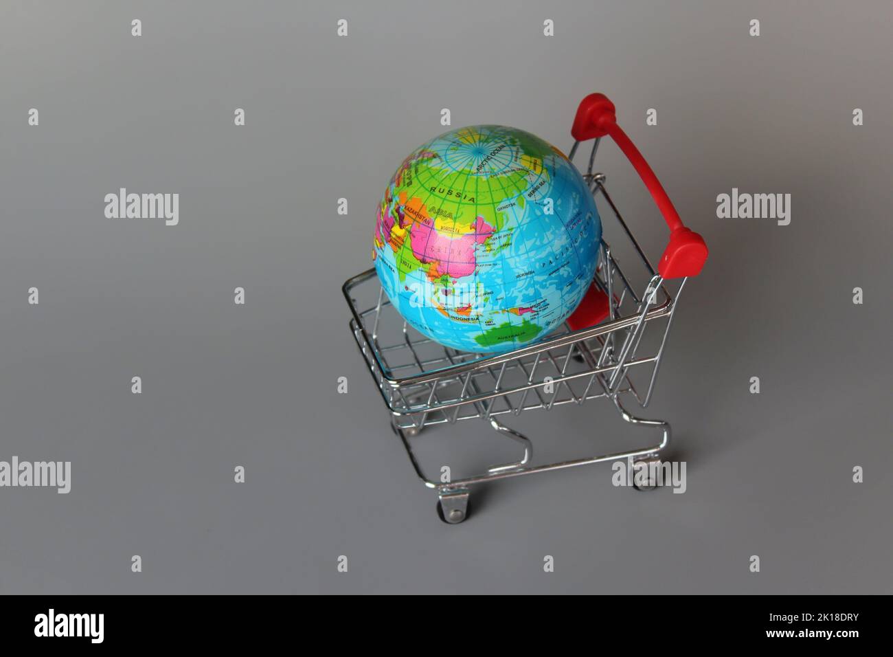 Mercato globale, concetto di mercato internazionale. Mini carrello e globo su sfondo grigio Foto Stock