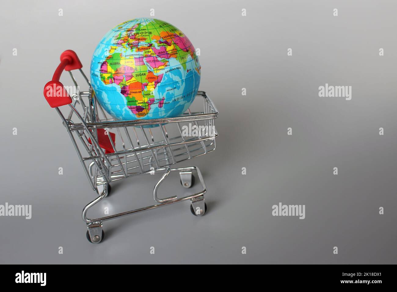 Mercato globale, concetto di mercato internazionale. Mini carrello e globo su sfondo grigio Foto Stock