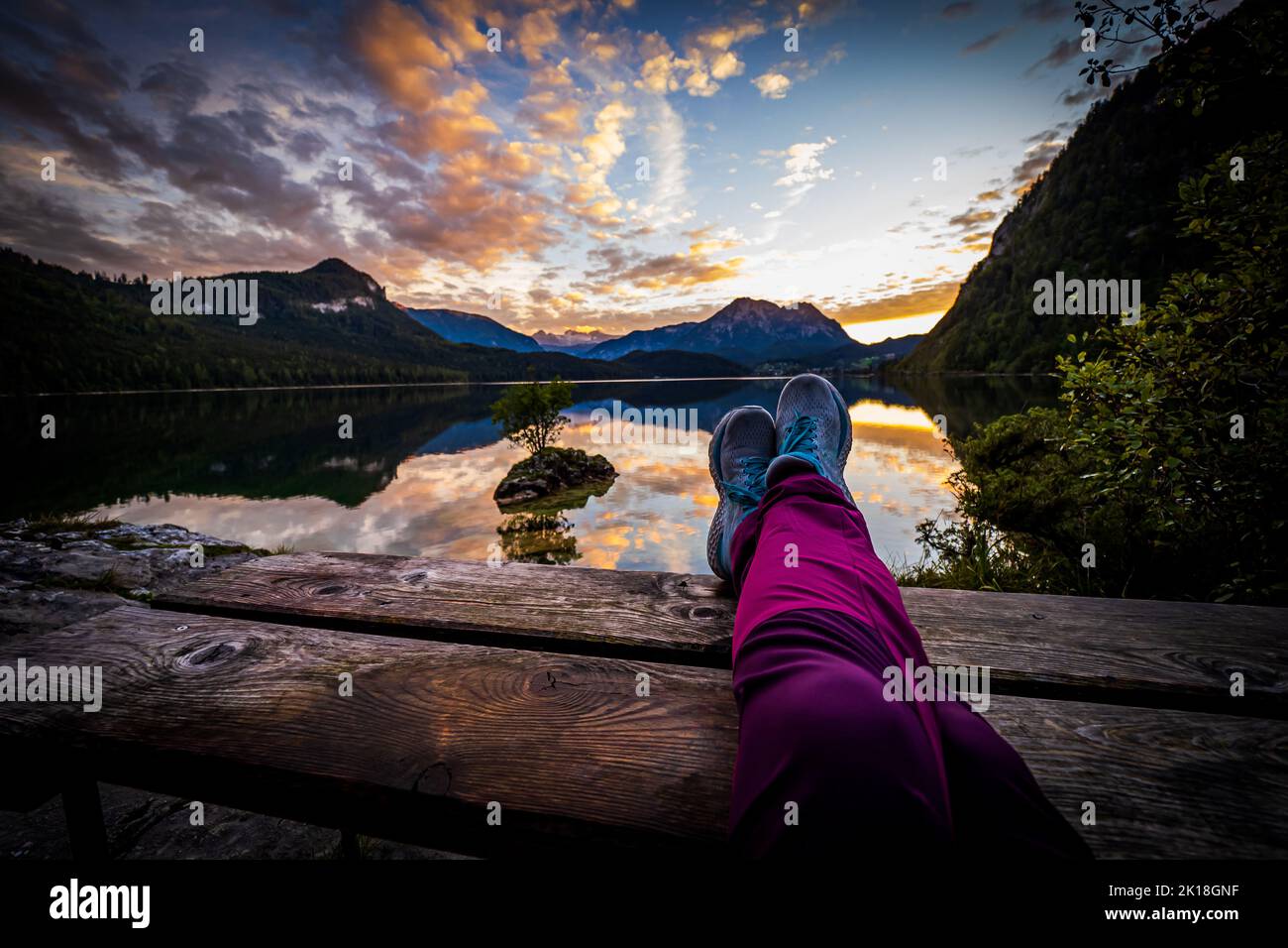 Escursionista femminile con gambe su un tavolo da picnic di fronte a una vista mozzafiato del tramonto di Altausseer See (Lago Aussee) nella regione di Ausseer Land, Stiria, Austria Foto Stock