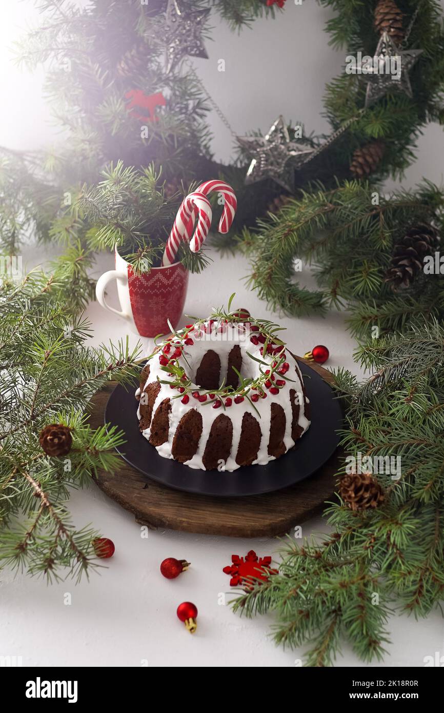 Cibo di Natale. Torta rotonda con glassa bianca. Cupcake con buco al centro con melograno. Rami di abete rosso verde sul tavolo. Vita morta. Dolci, dolci e dolci per il nuovo anno. Foto Stock