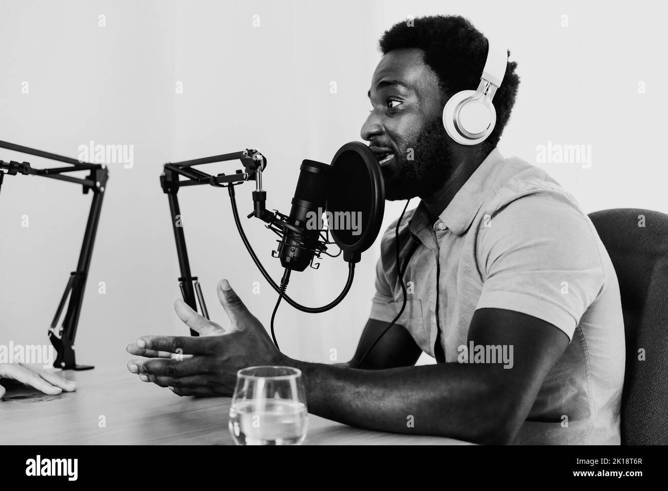 Uomo africano che registra un podcast utilizzando microfono e cuffie dal suo studio di casa - montaggio in bianco e nero Foto Stock