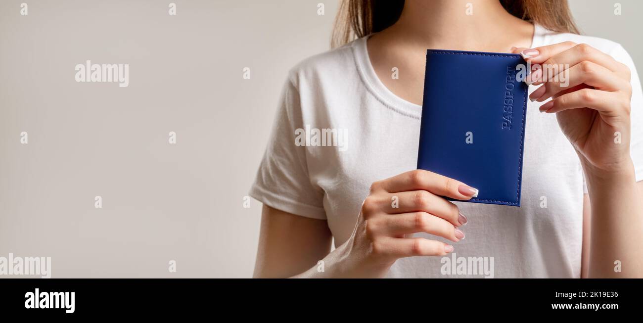 Servizio passaporti. Permesso di soggiorno. Donna in t-shirt bianca con documento d'identità nazionale in copertina blu isolata su sfondo nero neutro. Cent. Visa Foto Stock