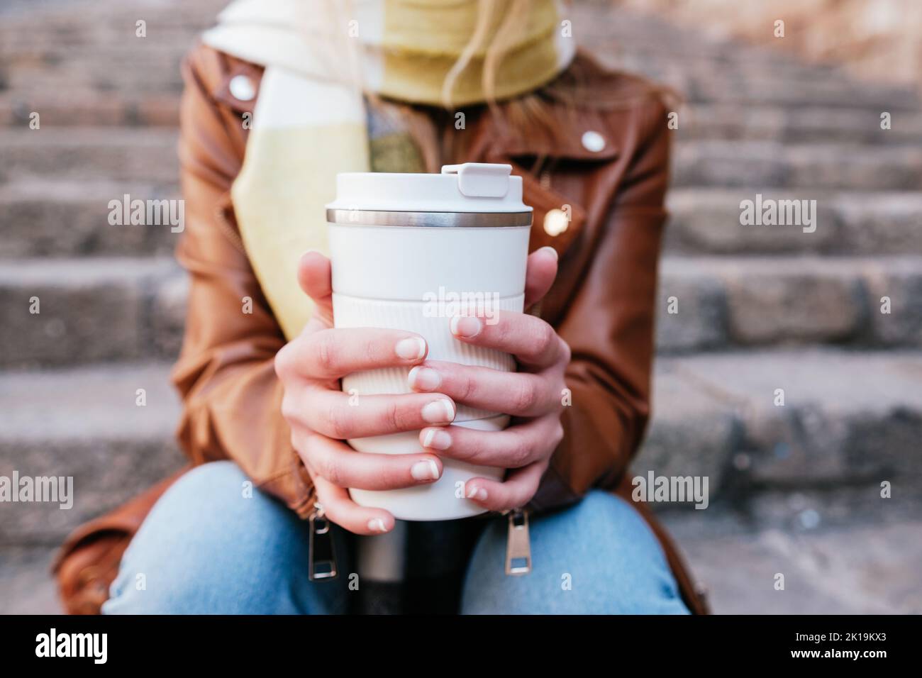 Giovane donna irriconoscibile con thermo tazza di caldo caffè da asporto seduto su gradini di pietra sulla strada della città Foto Stock