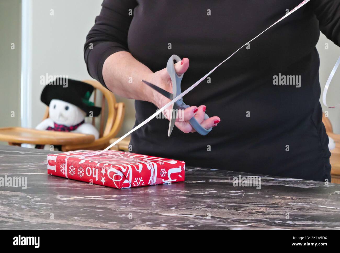 La mano delle donne usa le forbici per tagliare un nastro di un Natale avvolto o di un altro regalo di festa. Avvolgimento rosso e bianco, nastro e forbici in hobby fai da te. Foto Stock