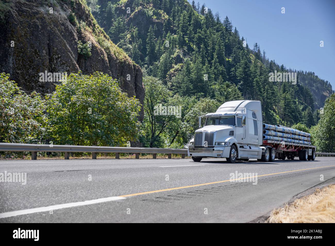 Industriale grande carro di perforazione bianco classico semirimorchio trasporto di tubi fissati sul pianale semirimorchio guida su strada con la montagna e per Foto Stock