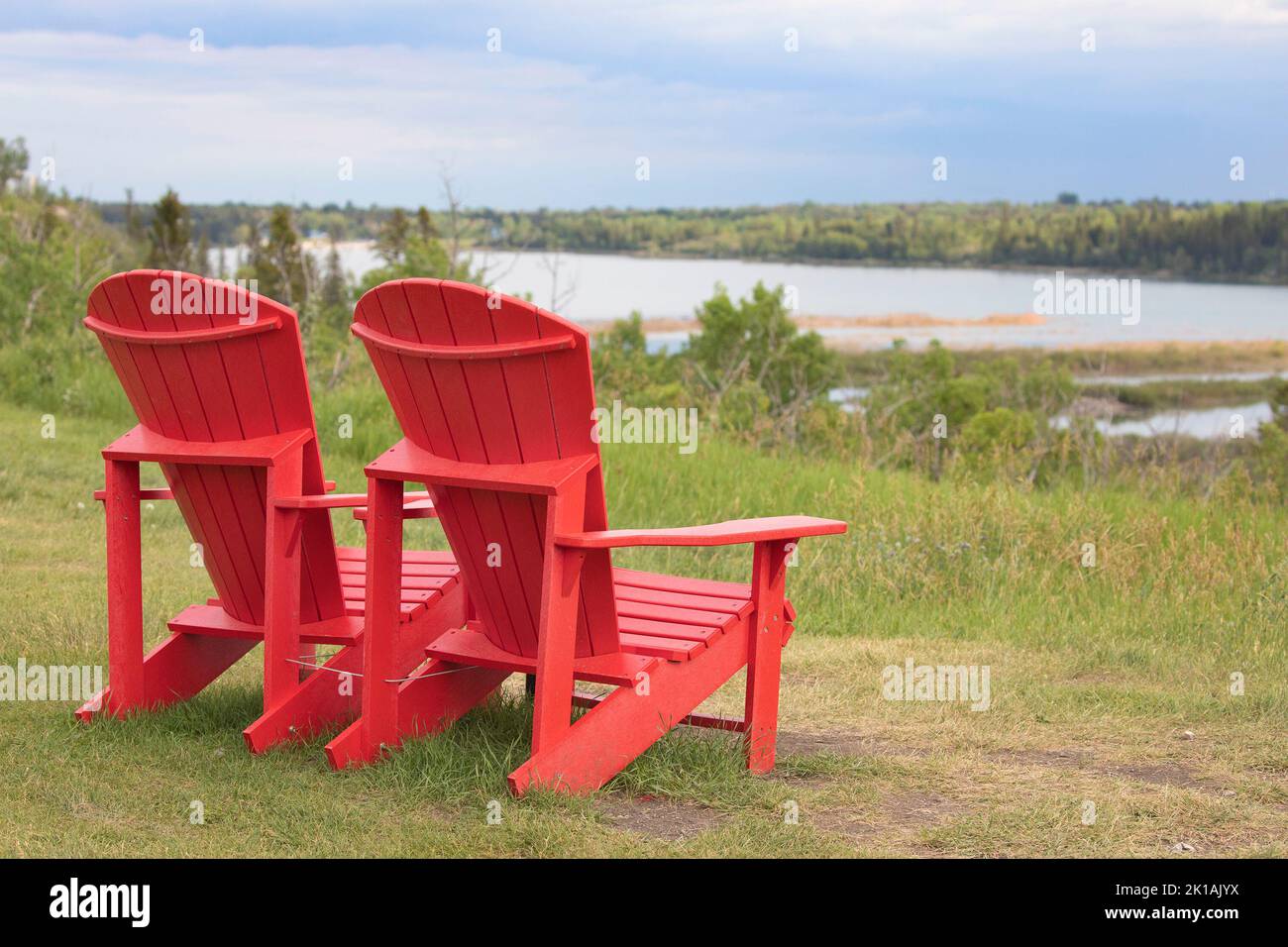 Sedie rosse adirondack che si affaccia su un lago a Weaselhead Flats, una zona naturale a Calgary, Alberta, Canada Foto Stock