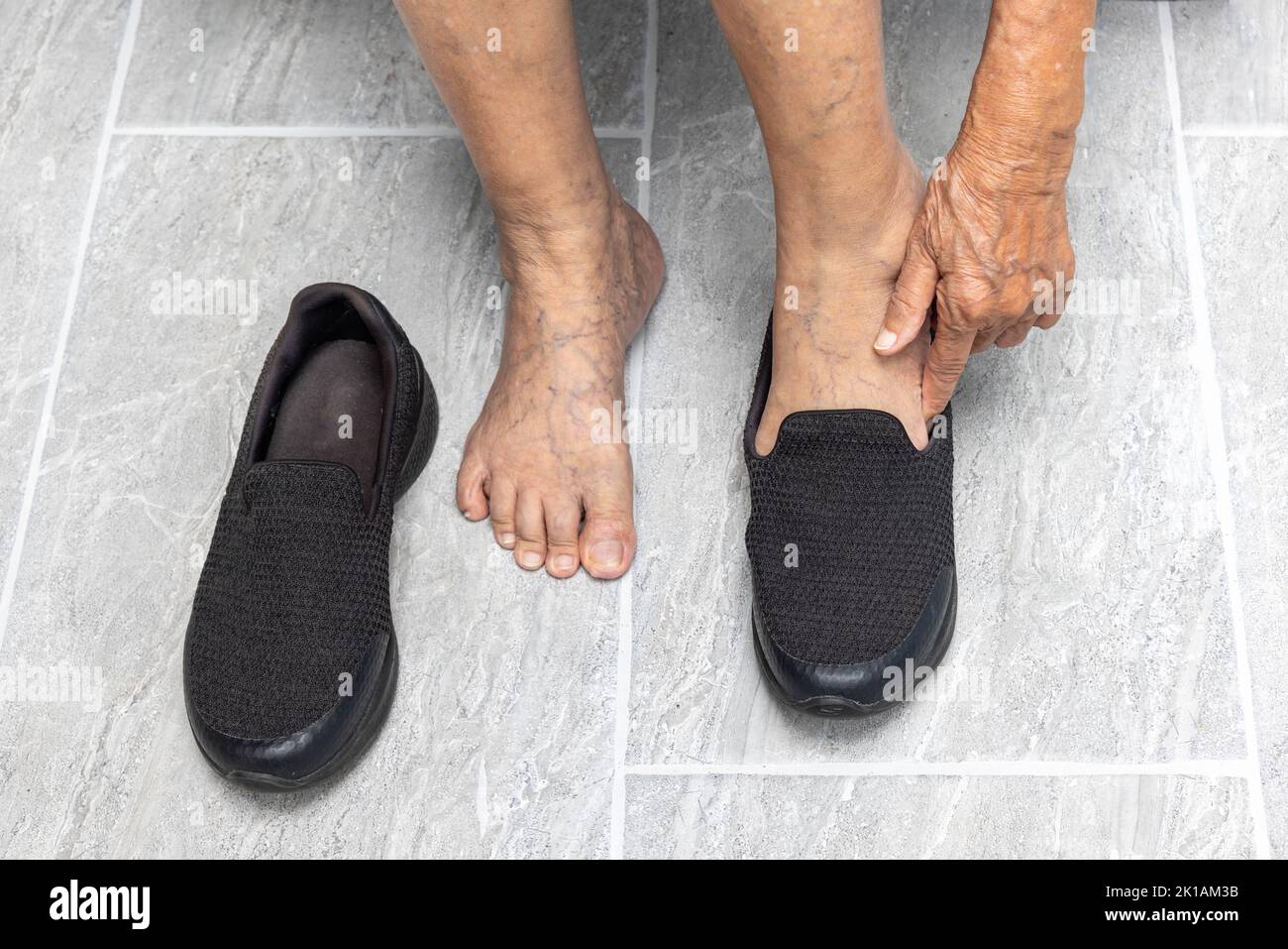 Donna anziana varicose vene piedi mette su una scarpa a casa. Foto Stock