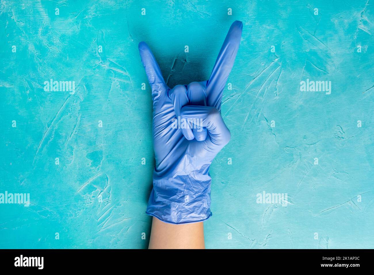 Prevenzione di Covid-19. Massima sicurezza. Mani in guanti medicinali che mostrano un gesto del corno sullo spazio di copia blu. Protezione da pandemia. Interrompa il coronavirus. Misuratore di igiene Foto Stock