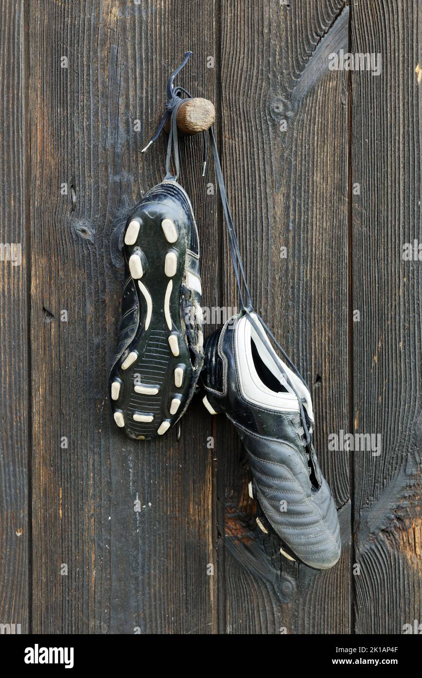 Un paio di stivali da calcio appesi su un muro di legno. La fine della carriera calcistica Foto Stock