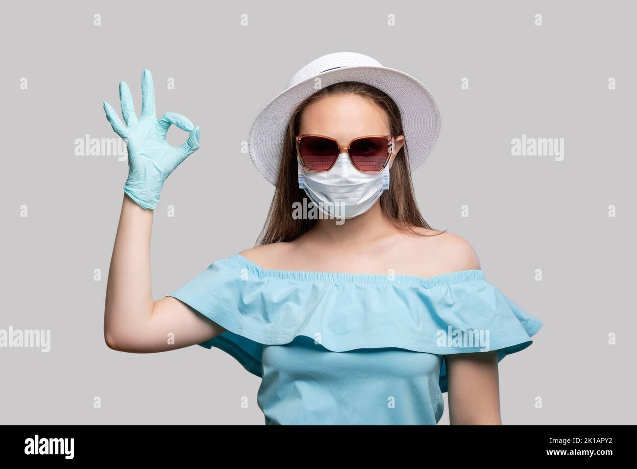 Protezione da virus. Prevenzione COVID-19. Donna salvata da maschera di medicina e guanti firma OK. Isolato su grigio. Pandemia di coronavirus. Strozzatura di traslazione Foto Stock
