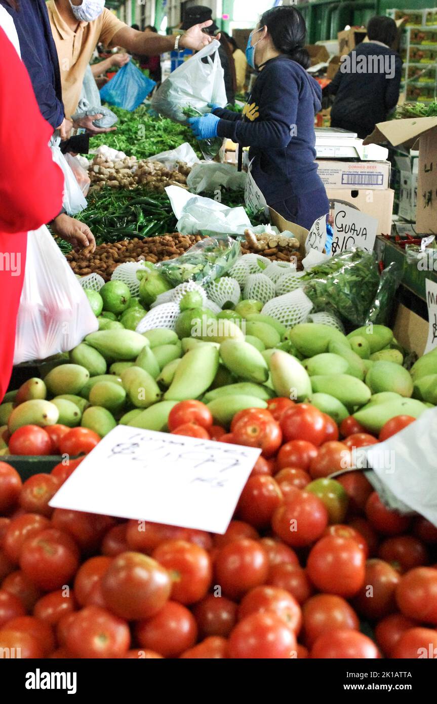 Un venditore al Paddy’s Market di Flemington, Sydney, che vende manghi verdi, pomodori, mele Granny Smith, fagioli e altri prodotti freschi di frutta e verdura Foto Stock