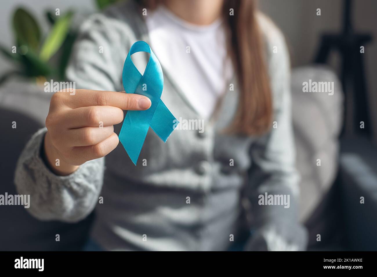 Simbolo per gli uomini di supporto. Primo piano della mano femminile che mostra un piccolo nastro blu seduto su un comodo divano. Messa a fuoco selettiva. Assistenza sanitaria, uomini internazionali, Foto Stock