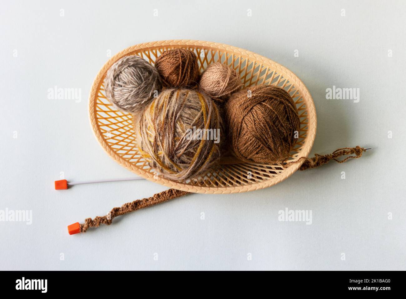 Palle di filo beige e marrone in un cesto beige con aghi per la lavorazione a maglia di abiti caldi, hobby per la lavorazione a maglia Foto Stock