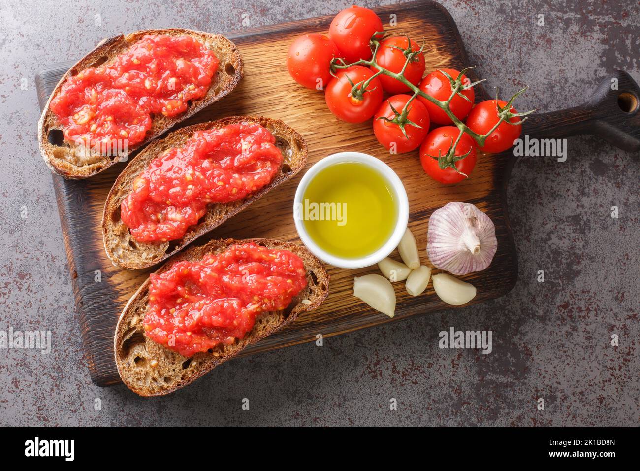 Pan Catalan con Tomate pane tostato spagnolo strofinato con aglio fresco e pomodoro maturo, poi sgocciolato con olio d'oliva spicchio sulla tavola di legno sul Foto Stock