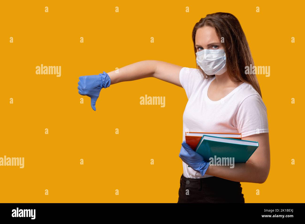 Restrizione quarantena. Protesta pandemica. Donna scettica in maschera protettiva guanti con pollice verso il basso gesto isolato su luminoso arancione copia spazio Foto Stock