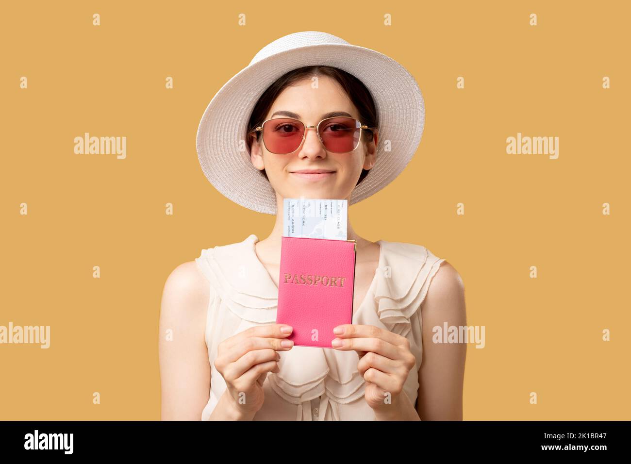 Vacanza prevista. Agenzia di viaggi. Vacanze estive. Donna felice in possesso di passaporto straniero con biglietti che guardano la fotocamera isolato su beige. Foto Stock