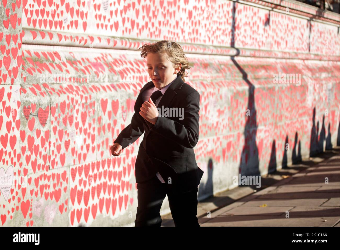 Westminster, Londra, Regno Unito. 16th Set, 2022. Un bambino in un vestito lutto corre accanto ai cuori dipinti sul muro commemorativo di Covid sull'Embankment di Londra mentre sua madre attende in fila per dire Arrivederci alla regina Elisabetta II Una stretta sicurezza è stata imposta in tutto il centro di Londra con una pesante presenza della polizia mentre la città si prepara per i funerali di sua Maestà la Regina Elisabetta II La Regina sarà sepolta lunedì 19th settembre. (Foto di Charlie Varley/Sipa USA) Credit: Sipa USA/Alamy Live News Foto Stock