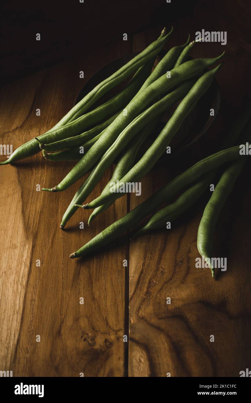 fagiolini verdi su una superficie di legno, noti anche come fagiolini, fagiolini o fiocchi, verdure raccolte di recente prese in fondo scuro Foto Stock