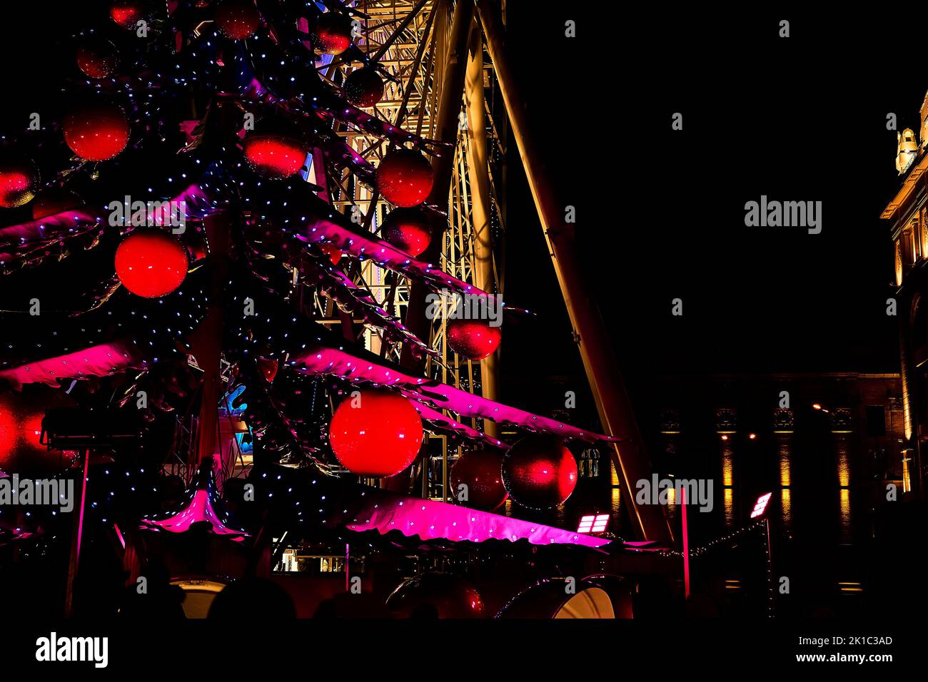 Albero di Natale con palline rosse, ali rosa. Ruota ferris incandescente, casa notte Foto Stock