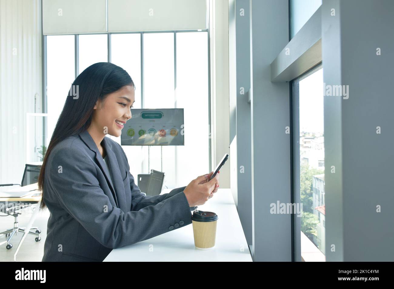 Felice donna asiatica senza busimess bere caffè caldo e ha usato il telefono cellulare con il tempo di relax in ufficio Foto Stock